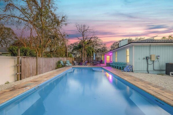 A swimming pool with a wooden deck, a wooden fence, and a building with a light blue exterior.