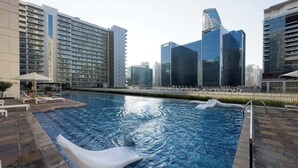 A swimming pool with a wave feature, surrounded by modern buildings and a clear sky.