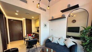 A modern living room with a sofa, coffee table, and a TV. There is a dining area with a table and chairs, and a kitchen in the background.