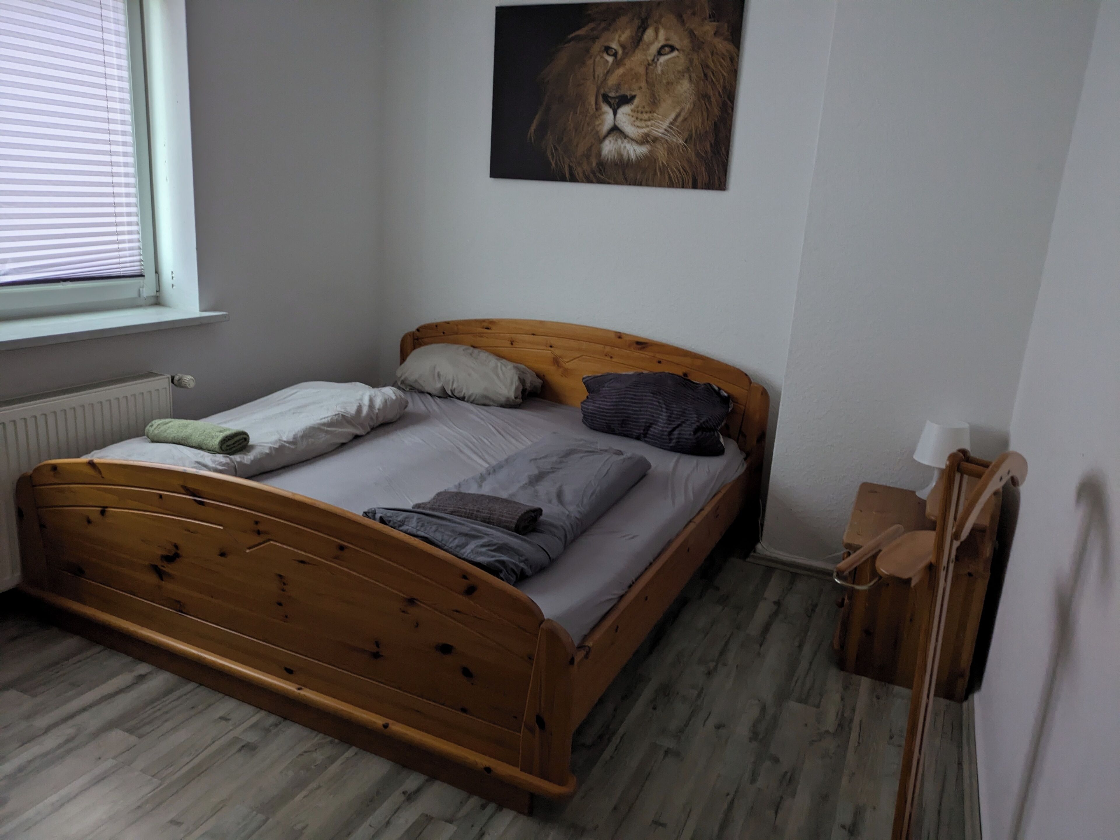 Un dormitorio con cama de madera, ropa de cama gris, almohada, manta y mesita de noche de madera con una lámpara.