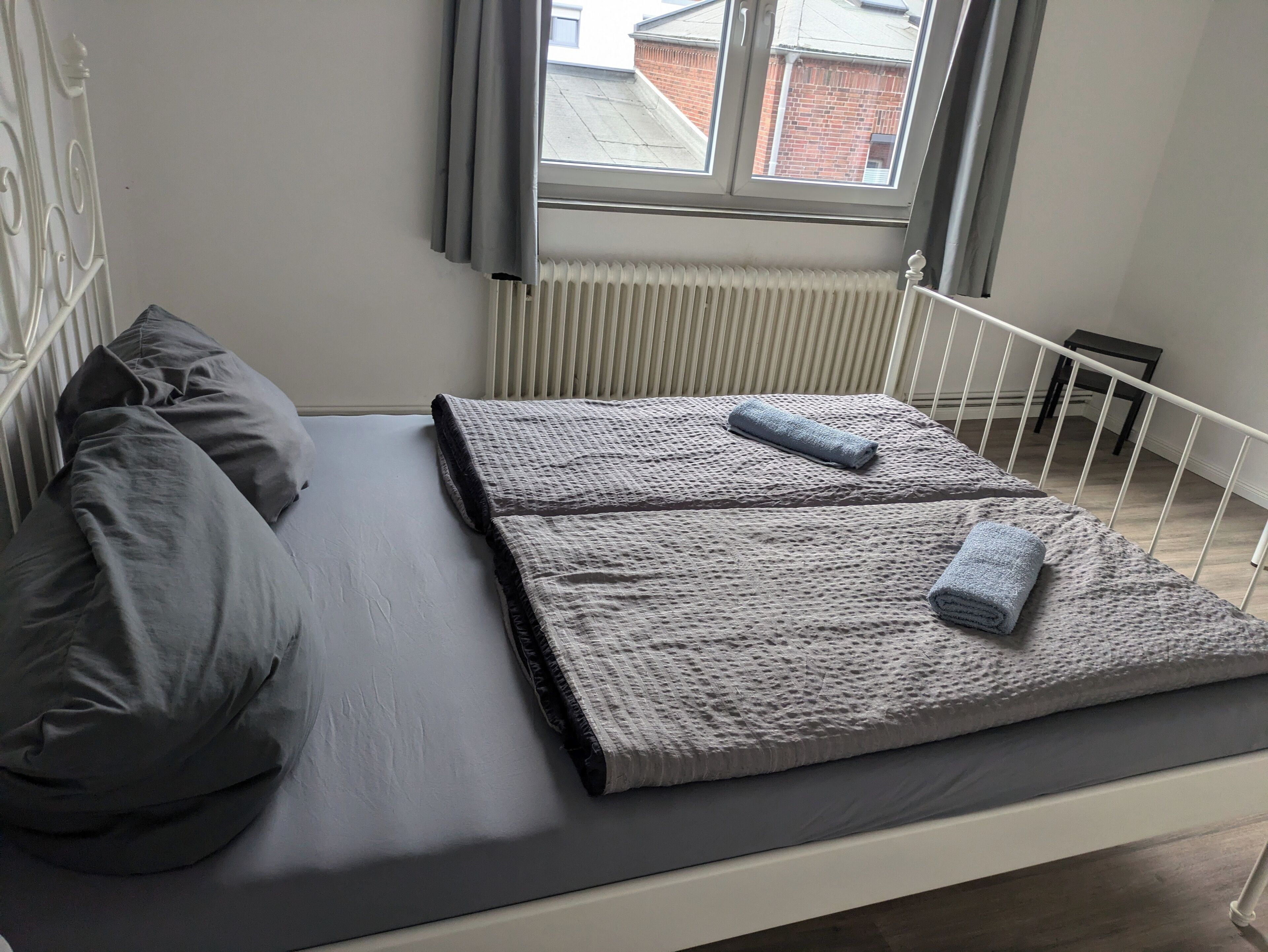 Un letto con biancheria grigia, una finestra con tende e un termosifone.