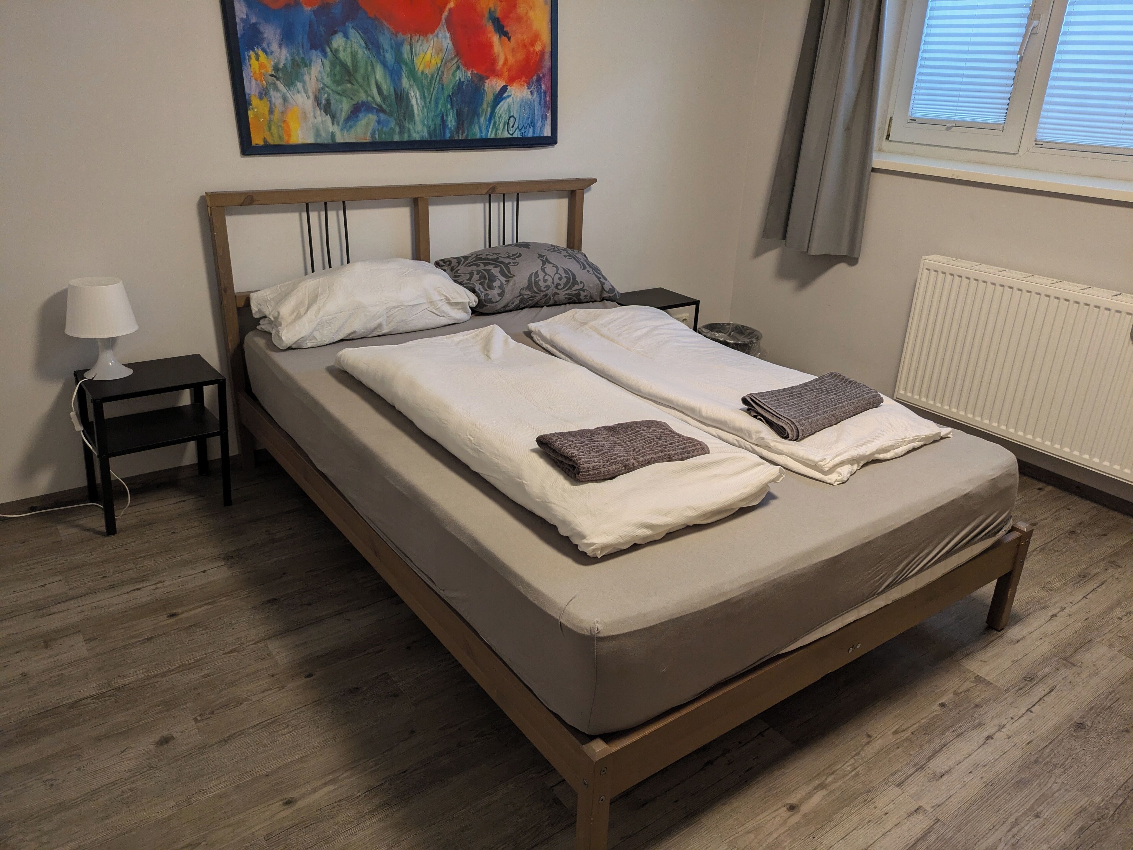 Un lit double avec un cadre en bois, deux oreillers, une table de chevet avec une lampe et un radiateur.