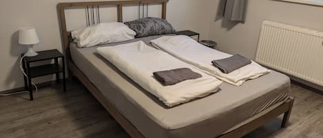 Un lit double avec un cadre en bois, deux oreillers, une table de chevet avec une lampe et un radiateur.