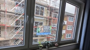 A window with a view of a building under construction, a sign advertising a job, and a radiator below. - NestOaseWHV Zimmer zw.City und Südstrand (Wilhelmshaven)
