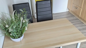 A small dining area with a wooden table, two black chairs, and a potted plant with green foliage. - NestOaseWHV Zimmer zw.City und Südstrand (Wilhelmshaven)