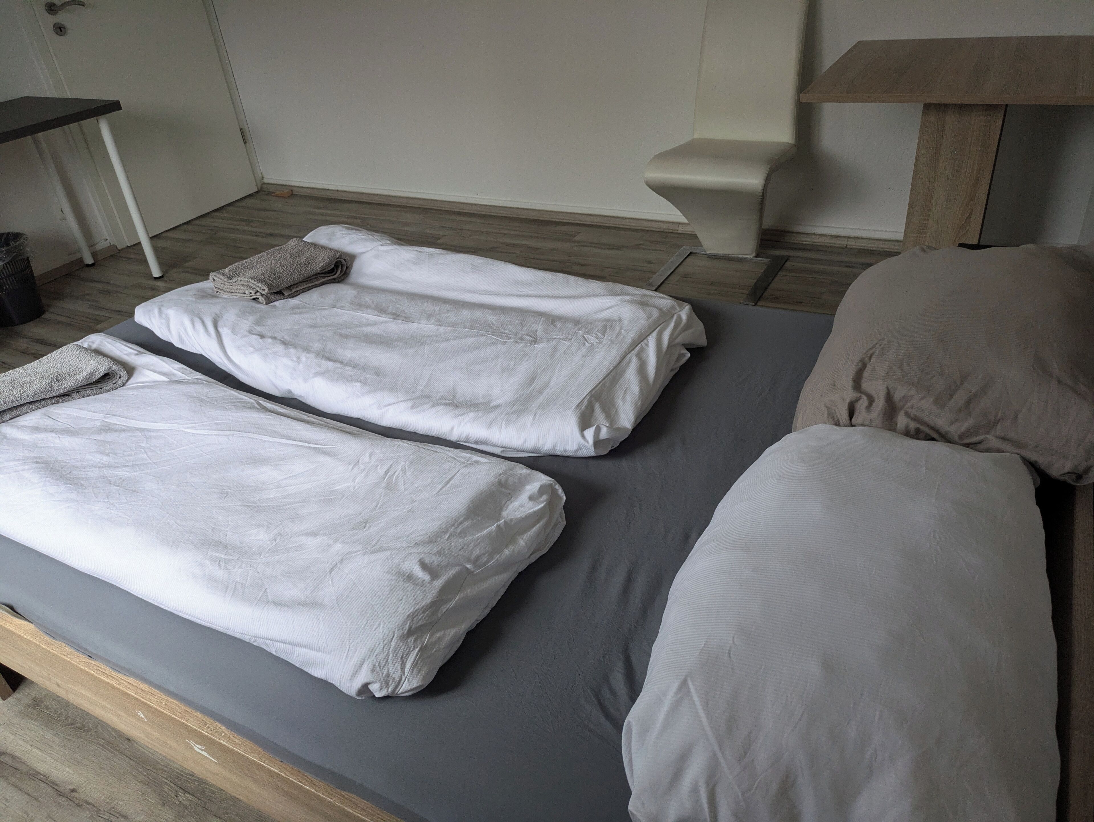 A room with two single beds, a small table, a chair, and a bedside table.