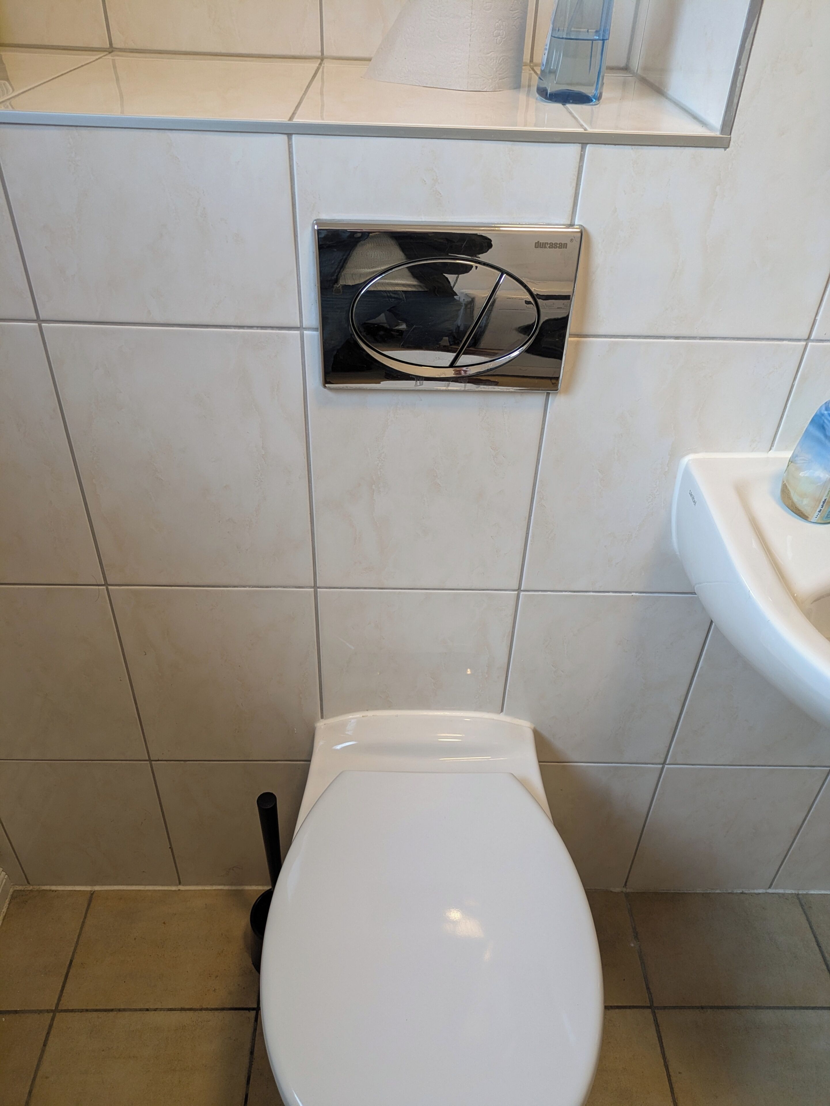 Un baño con inodoro blanco, dispensador de toallas de papel y secamanos mural.