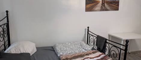 Un lit simple avec un matelas gris, un oreiller rayé et un oreiller blanc. Un tableau représentant un éléphant sur une route est accroché au mur.