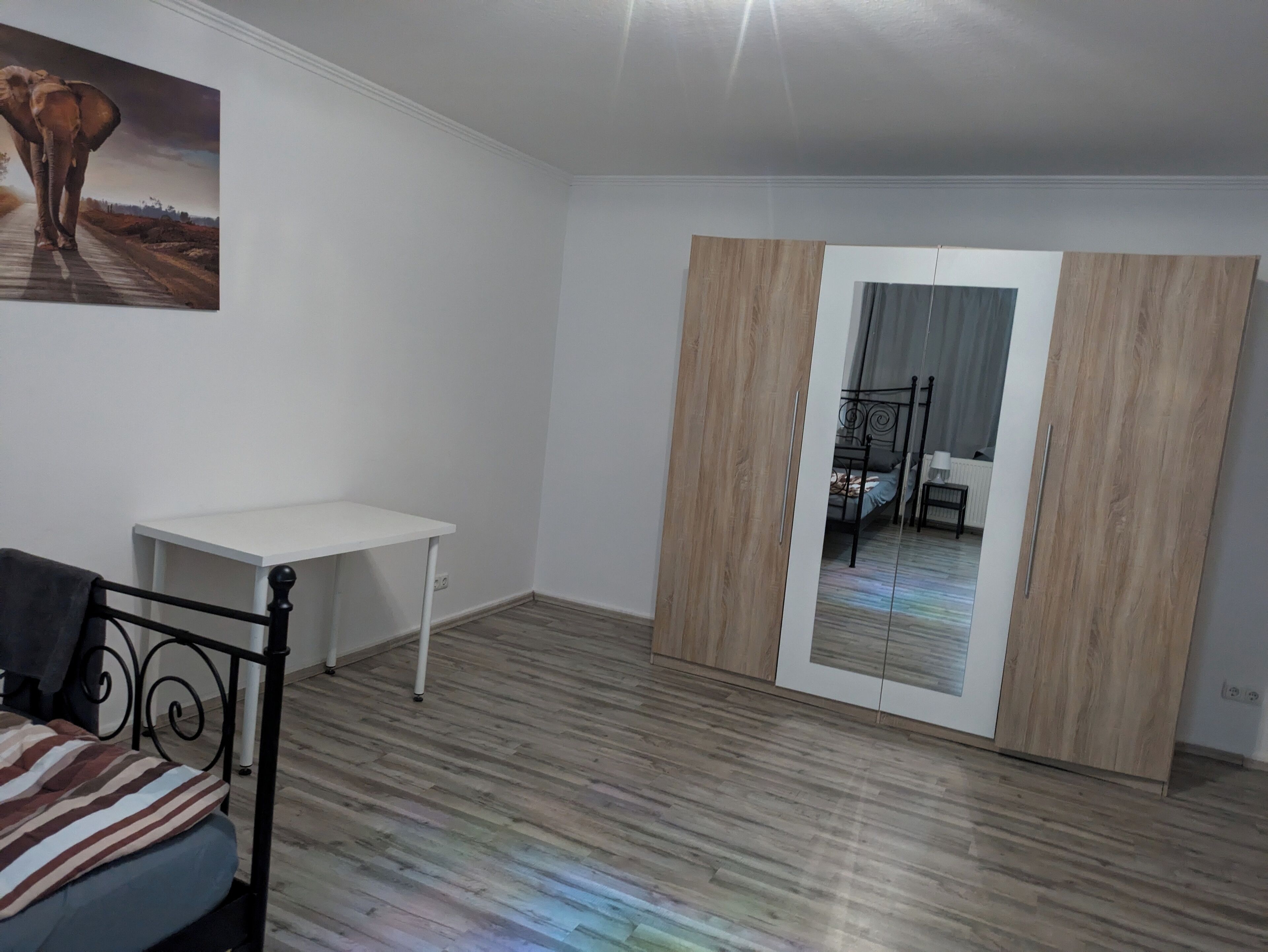 A bedroom with a bed, a small white table, a mirror, and a wardrobe.