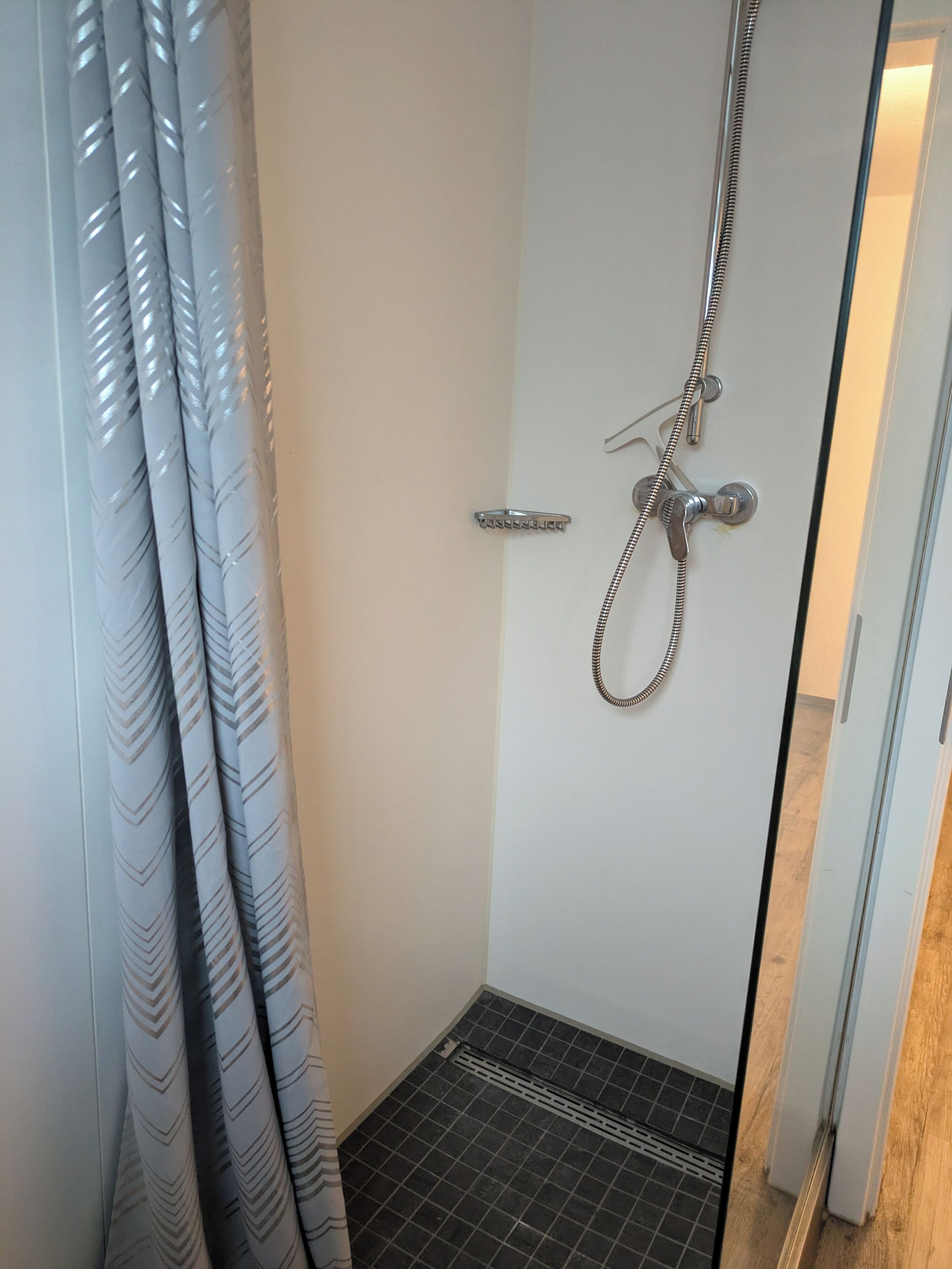 A small, enclosed shower area with a showerhead, a door handle, and a tiled floor.