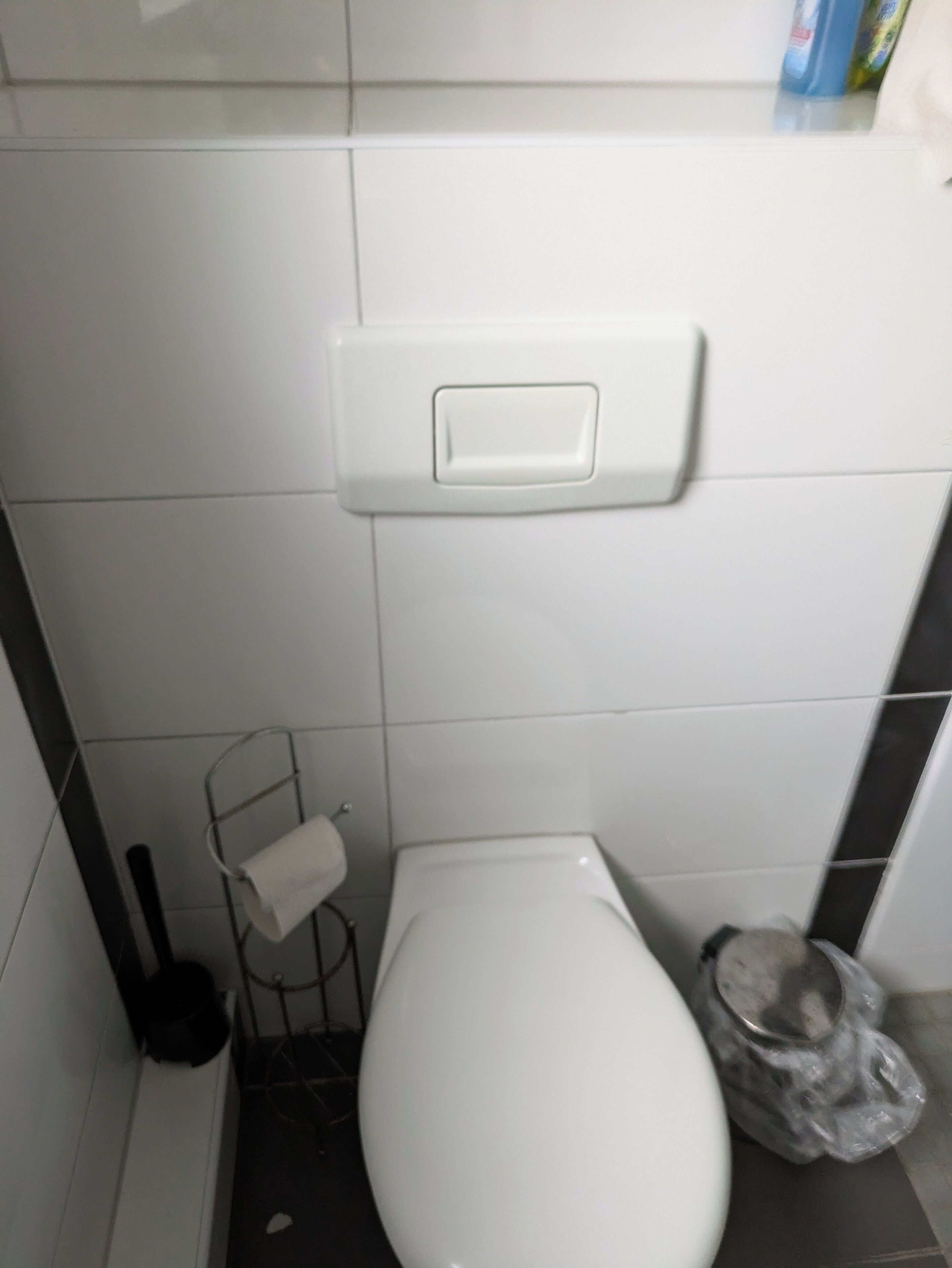 Pieni, valkoinen wc, jonka vasemmalla puolella on paperipyyheannostin ja oikealla puolella roskakori.