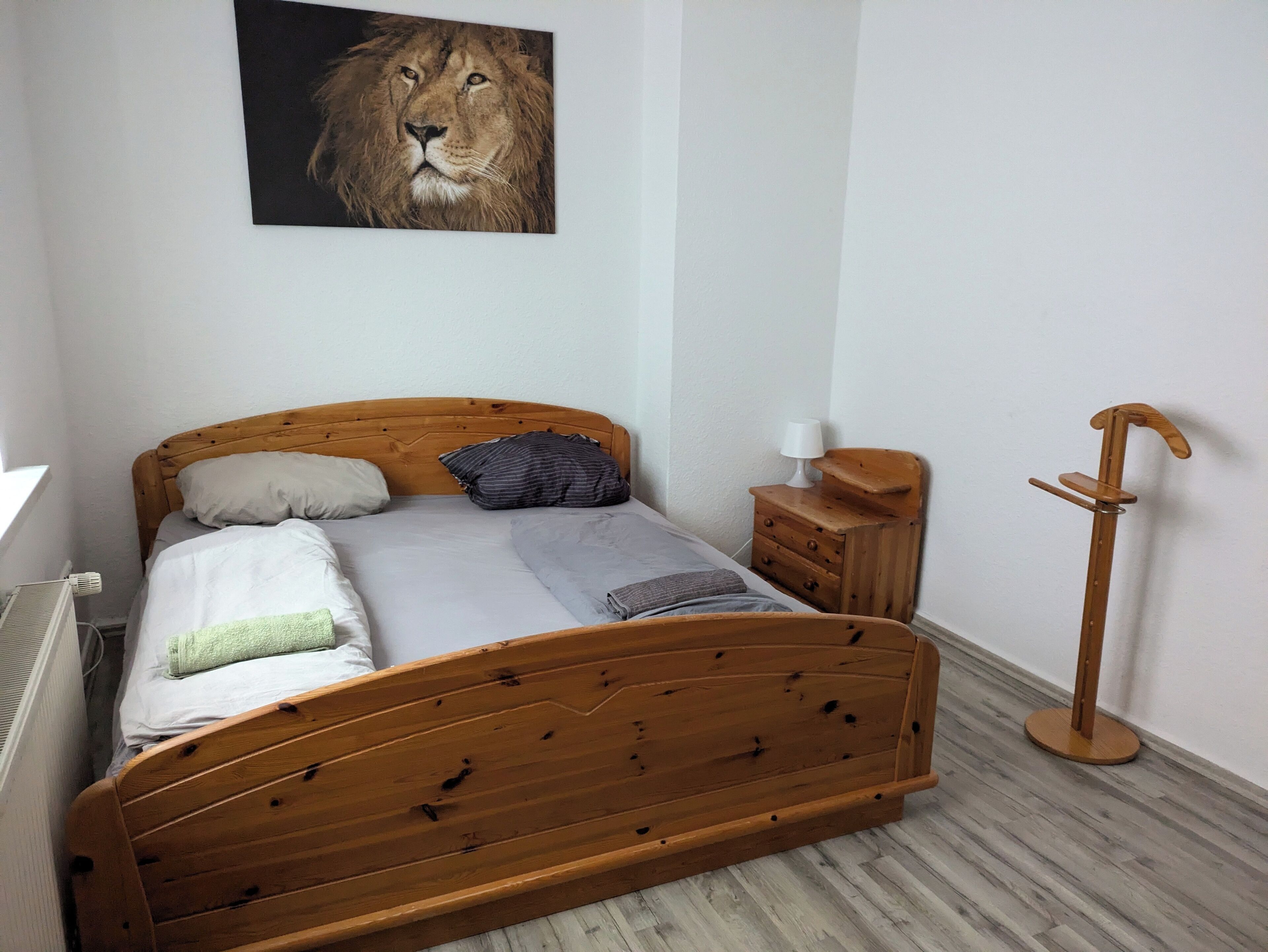A bedroom with a wooden bed, a nightstand, a lamp, and a wooden floor.