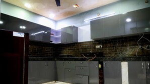 A kitchen with grey cabinets, a black countertop, and a brick backsplash. - The Sawera- Haridwar (Haridwar)