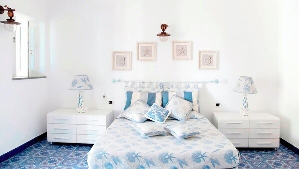 A bedroom with a bed, two nightstands, a window, and wall art. - VILLA ROCCE ROSSE (Lipari)