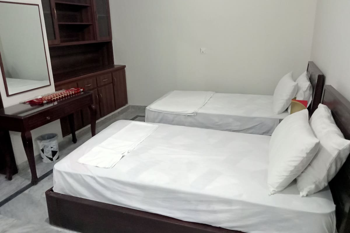 Ein Hotelzimmer mit zwei Einzelbetten, einem Holztisch mit Stuhl, einem Spiegel und einer kleinen Mülleimer.