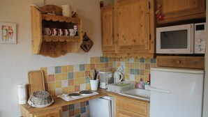 A kitchen with wooden cabinets, a microwave, a small refrigerator, and a tiled backsplash. - Joran JR7 Sunny & View 4 Pers (Chatel)