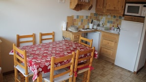 A small kitchen with wooden cabinets, a microwave, a refrigerator, and a dining table with chairs. - Joran JR7 Sunny & View 4 Pers (Chatel)