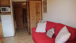 A red sofa with patterned pillows, a white refrigerator, and a wooden door in a room with tiled flooring. - Joran JR7 Sunny & View 4 Pers (Chatel)