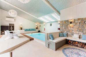 Un área interior de piscina moderna con pared de piedra, asientos y un techo con tragaluces.