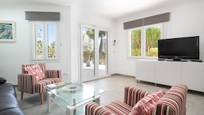 A modern living room with a glass coffee table, striped armchairs, a sofa, a flat-screen TV, and a sliding glass door leading to an outdoor area. - PLAYMAR (Alcúdia)