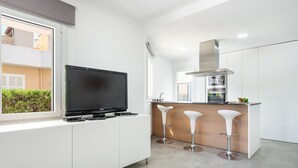 A modern kitchen with a built-in TV, a central island with stools, and a stainless steel range hood. - PLAYMAR (Alcúdia)