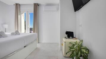 Een moderne hotelkamer met een bed, een televisie, een klein tafeltje met een plant en een raam met gordijnen.
