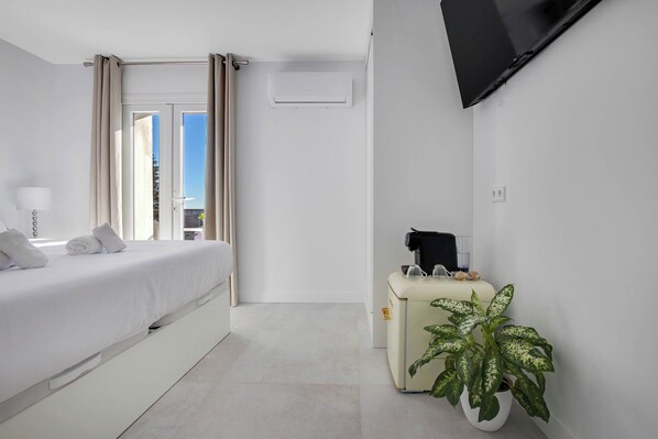 Habitación de hotel moderna con cama, televisión, una mesita con una planta y ventana con cortinas.