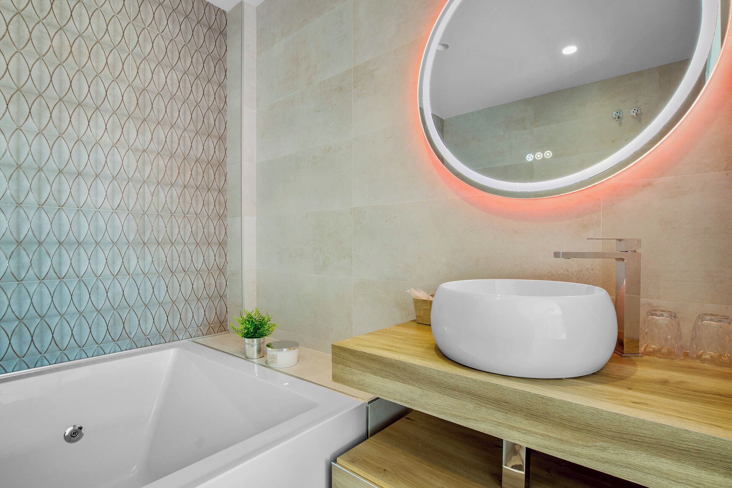Ein modernes Badezimmer mit einer großzügigen Badewanne, einem runden Spiegel mit roter Beleuchtung und einem Holzwaschtisch mit weißem Waschbecken.