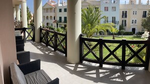 Un balcón con muebles de mimbre y vistas a un patio con edificios y palmeras.