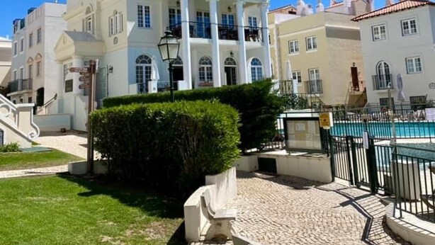 Un edificio blanco con un balcón central y una zona de piscina al frente.