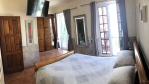 Un dormitorio con cama, armario de madera, televisor y baño con ducha.