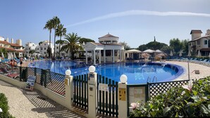 Una piscina rodeada de sillones de descanso, un pabellón y palmeras.