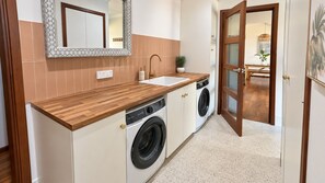 Eine kleine Küche mit Holzarbeitsplatte, Spüle, Waschmaschine und einer Tür zum Essbereich.