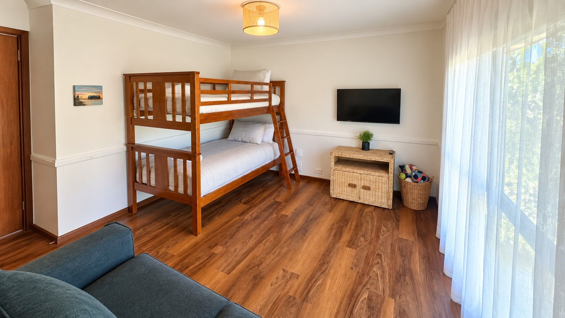 Une chambre avec un lit superposé, un téléviseur à écran plat, une petite table avec une plante et un panier en osier.