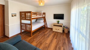 A room with a bunk bed, a flat-screen TV, a small table with a plant, and a wicker basket.