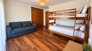 A room with a bunk bed, a sofa, wooden flooring, and a door.