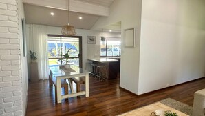 Een moderne keuken met een centraal eiland, een eethoek met tafel en stoelen, en een uitzicht op de omgeving door grote ramen.