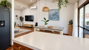 A modern kitchen with a large island, a flat-screen TV mounted on a white brick wall, and a hanging pendant light.