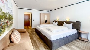 A modern hotel room with a large bed, a sofa, and a painting on the wall. - Comfortable and versatile room -perfect for relaxation, work and exchange (Winterberg)