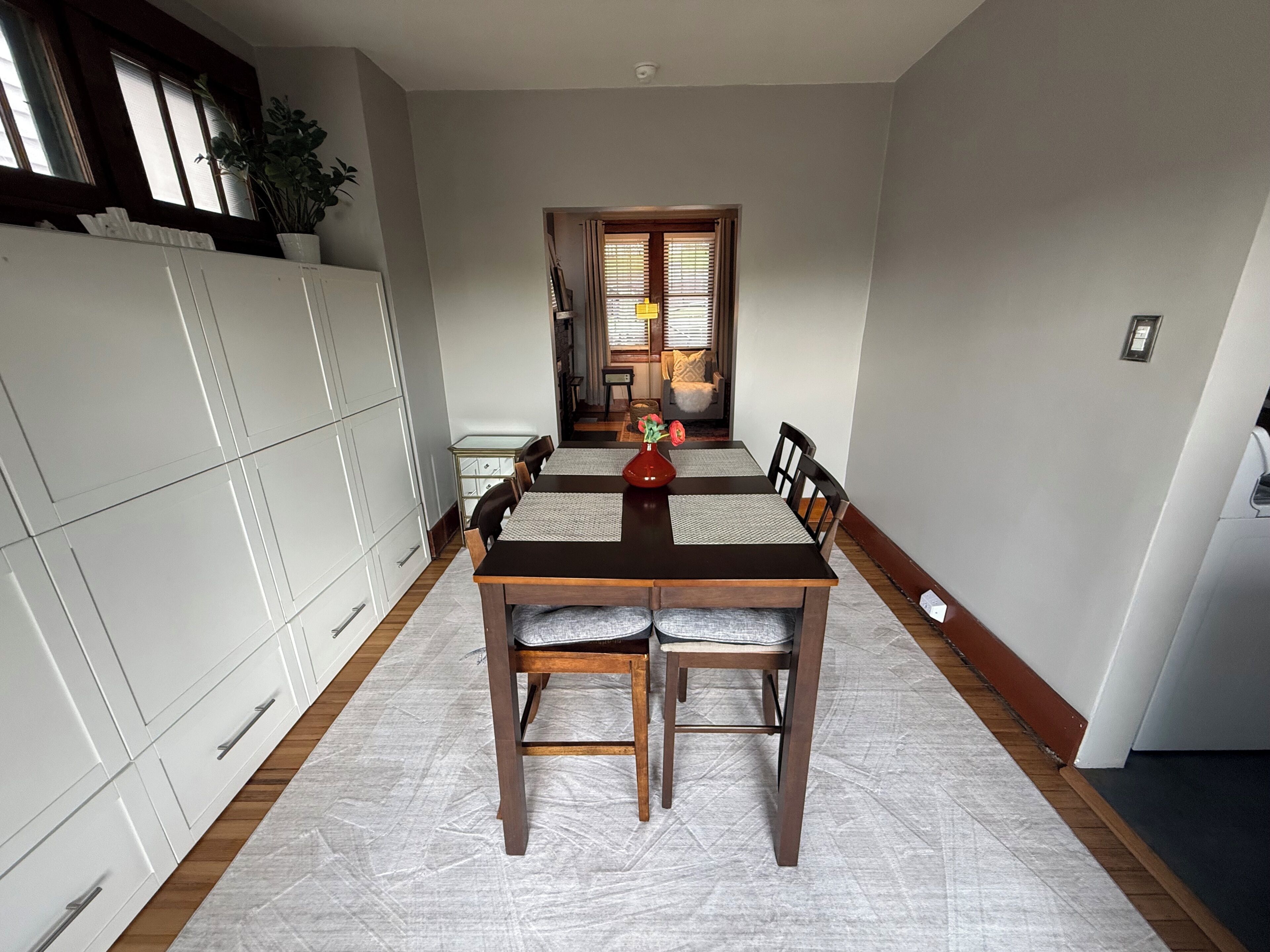 A dining area with a wooden table and chairs, a white cabinet, and a plant.