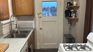 A compact kitchen with a gas stove, double sink, wooden cabinets, and a view through a window. - Pittsburgh city views close to all, cozy & bright 1BR - King + Dedicated Office (Pittsburgh)