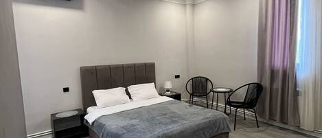 Un dormitorio con cama, mesitas de noche, una silla y una pequeña mesa.