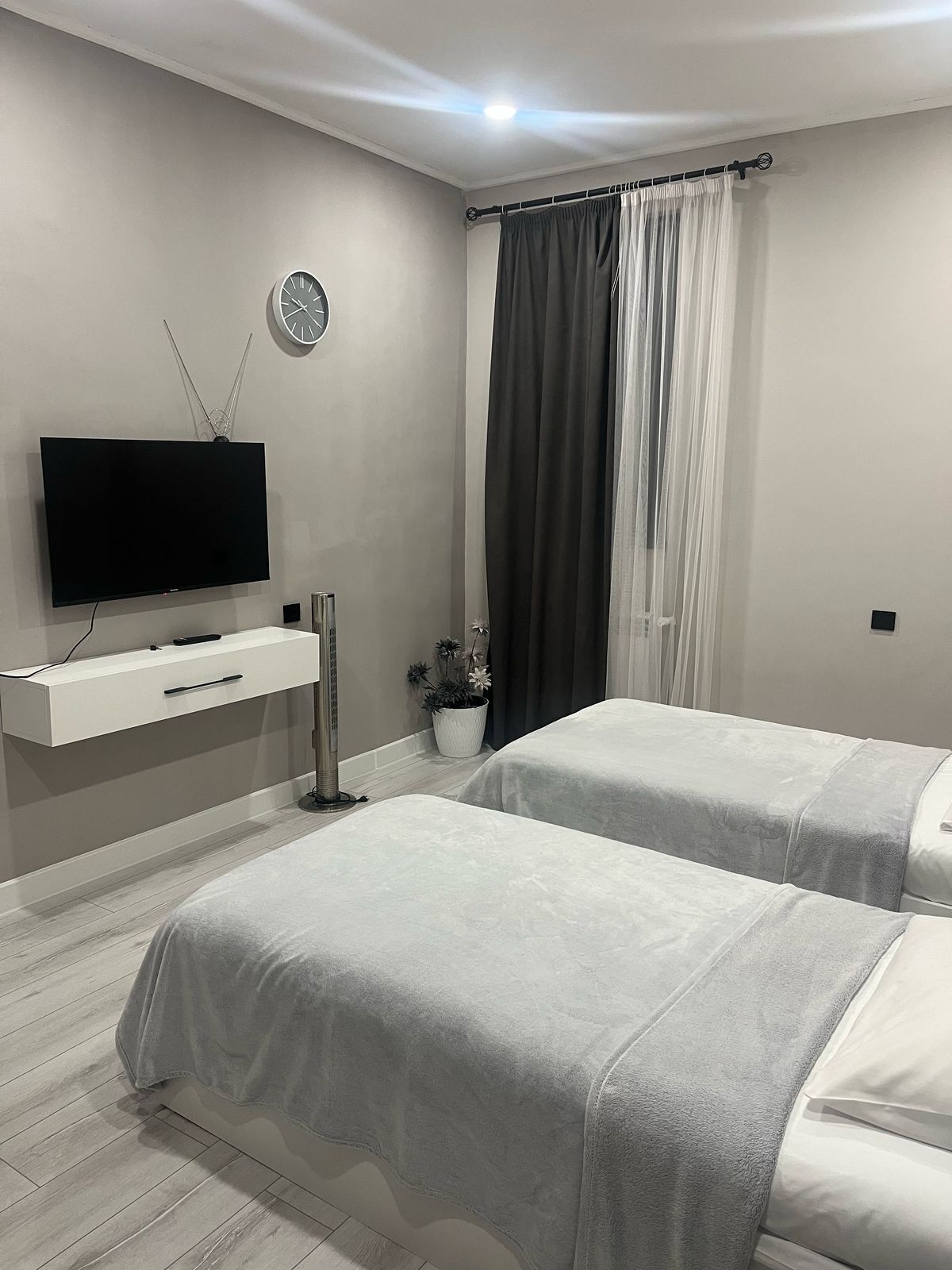 Una camera da letto moderna con due letti, una televisione, una sveglia e una pianta in vaso.