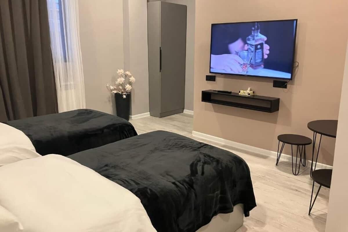 A hotel room with two beds, a TV mounted on the wall, a small table, and a chair.
