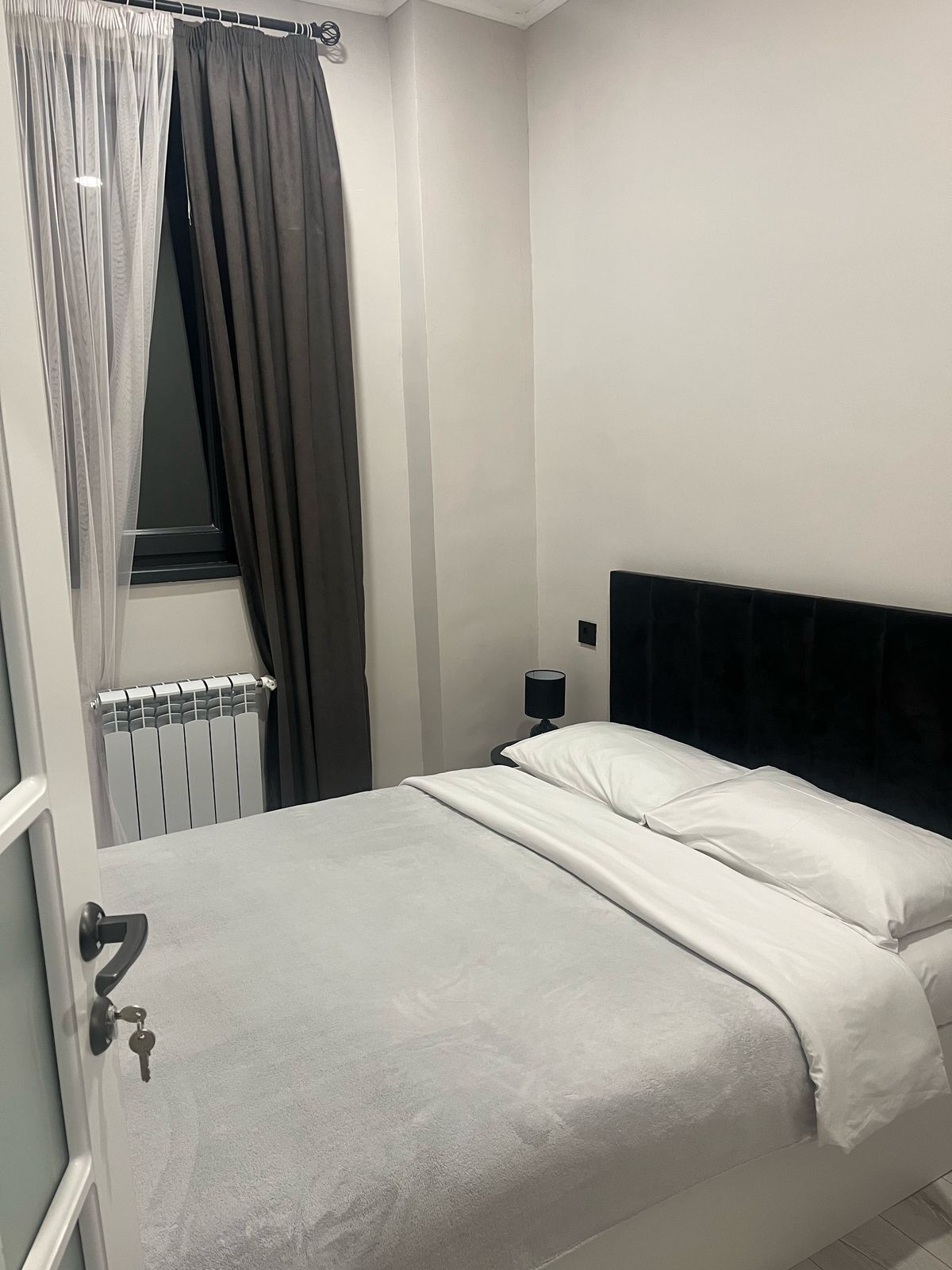 Une chambre à coucher avec un lit, une table de chevet, une fenêtre avec des rideaux et un radiateur.