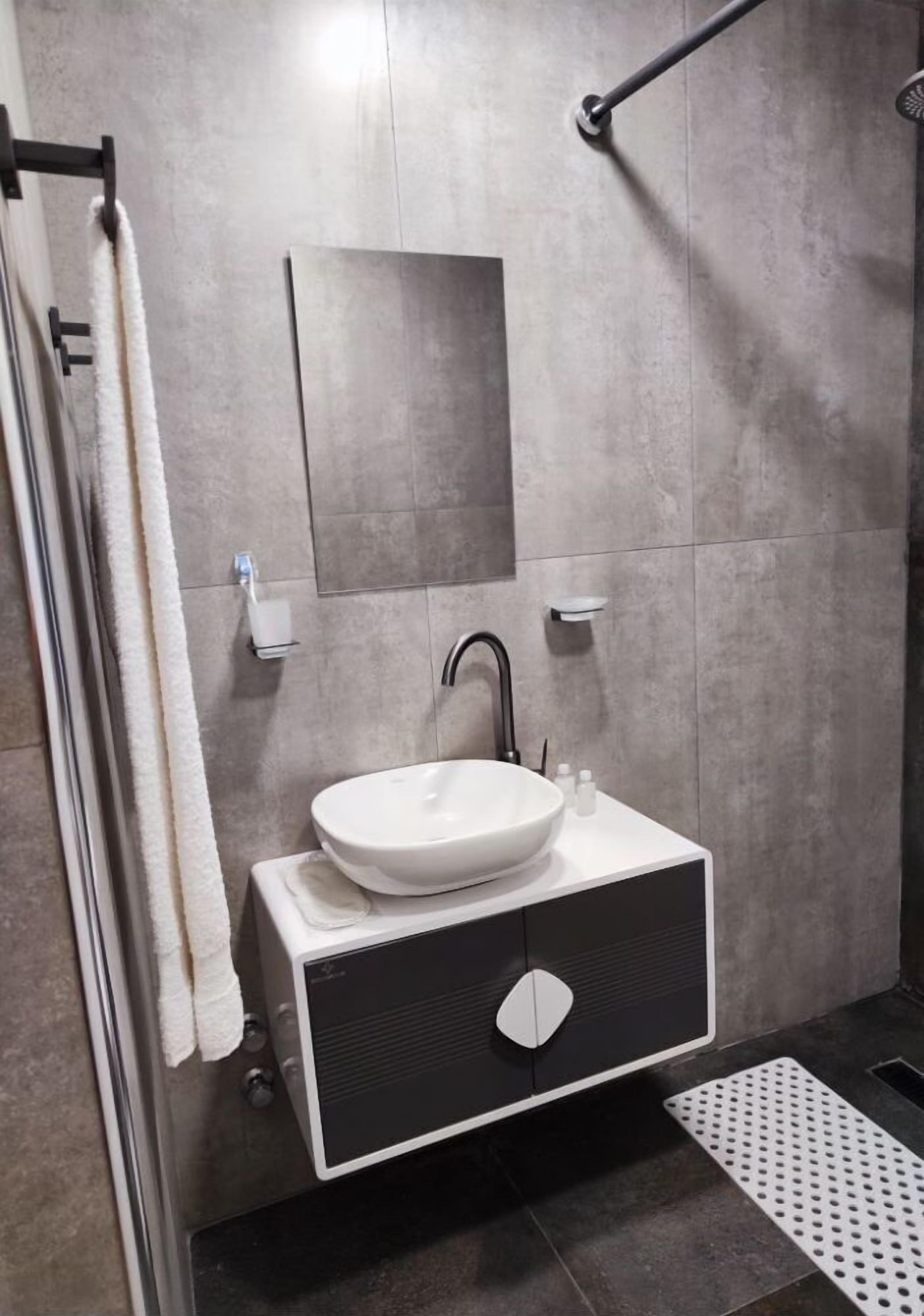 A modern bathroom with a large sink, a mirror, and a shower area.