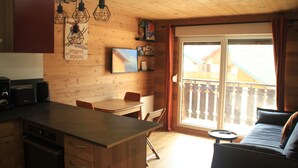 Ambiente interno in legno con angolo cottura, tavolo da pranzo e divano vicino a una porta vetrata scorrevole.