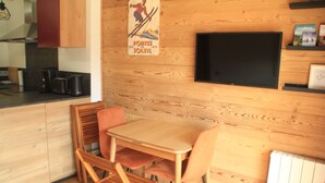 A wooden-paneled room with a table and chairs, a television mounted on the wall, and a kitchen area with appliances. - Veronica Vr51 Nature & Mountain 6 Pers (Chatel)