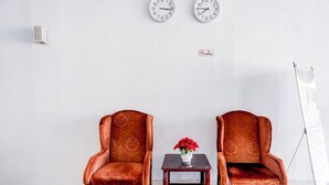 Deux fauteuils en velours, une petite table placée entre eux, une horloge au mur et un panneau indiquant qu'il est interdit de fumer.