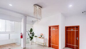 Un couloir avec deux portes en bois portant les numéros 201 et 202, une console blanche ornée d’objets décoratifs, une plante en pot et un extincteur.